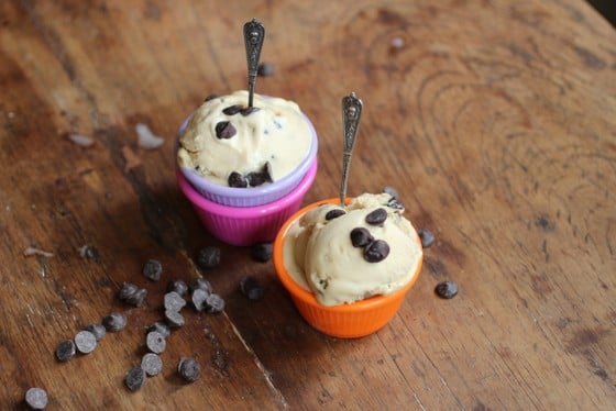 Top view of chocolate chip ice cream on colorful ramekins with spoons on a wooden table with scattered chocolate chips.