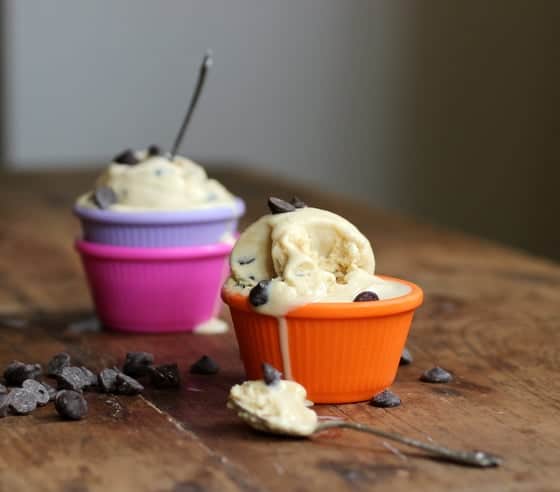 Chocolate chip cookie ice cream on colorful ramekins with spoons on a wooden table with chocolate chips.