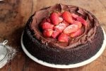 Whole chocolate cake with strawberries on white plate on a wooden table