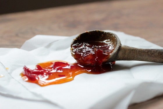Wooden spoon with Red Chile Jam on white paper and wooden table