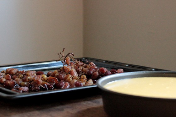 Baking tray with grapes and round pan with cheesecake on a wood and brown background.