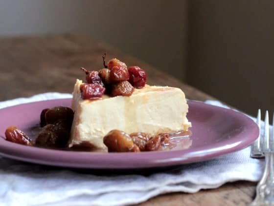 Purple plate with slice of cheesecake topped with grapes, white cloth, wooden table