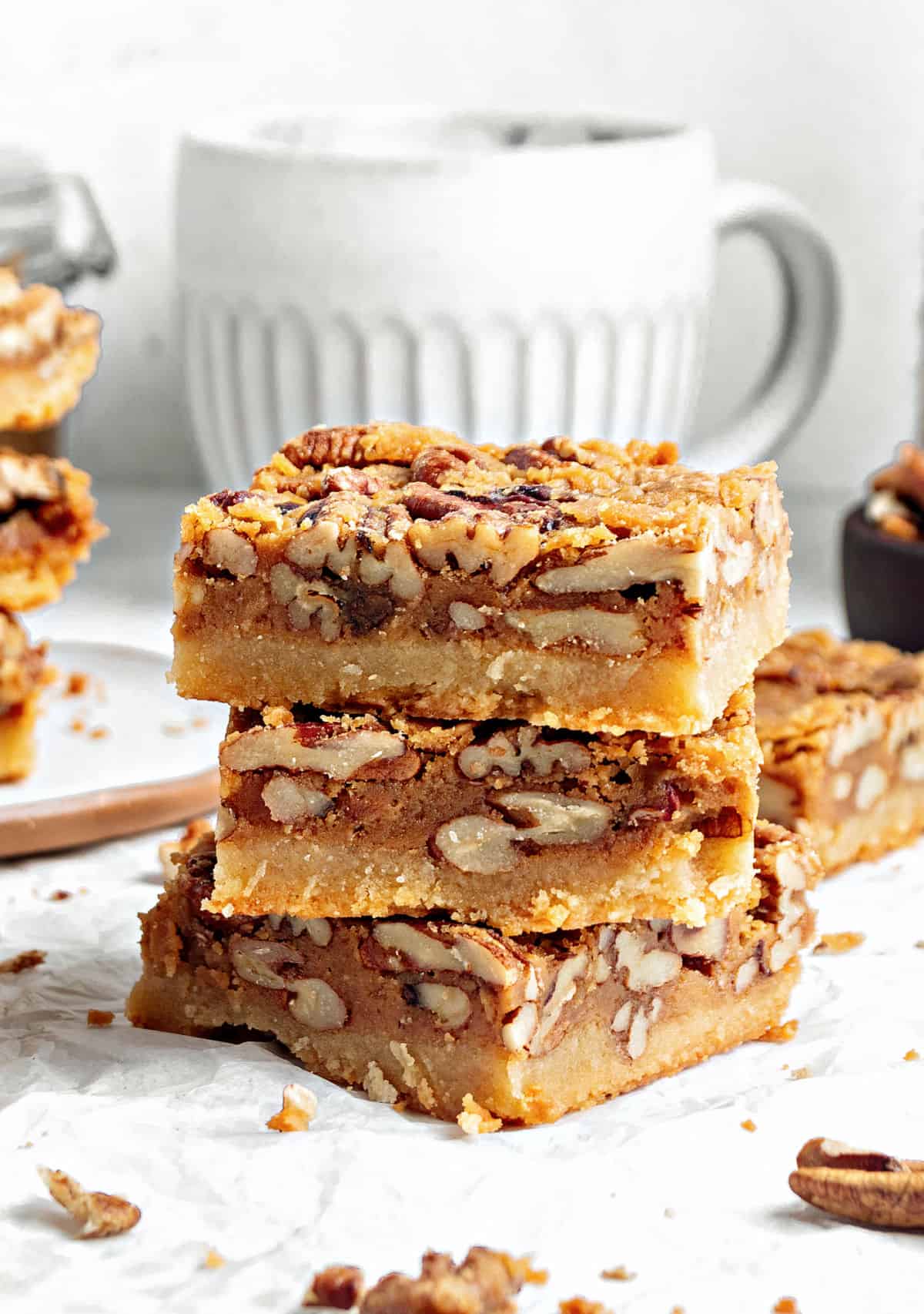 Stack of three pecan maple bars. White surface. White ceramic jug in the background.