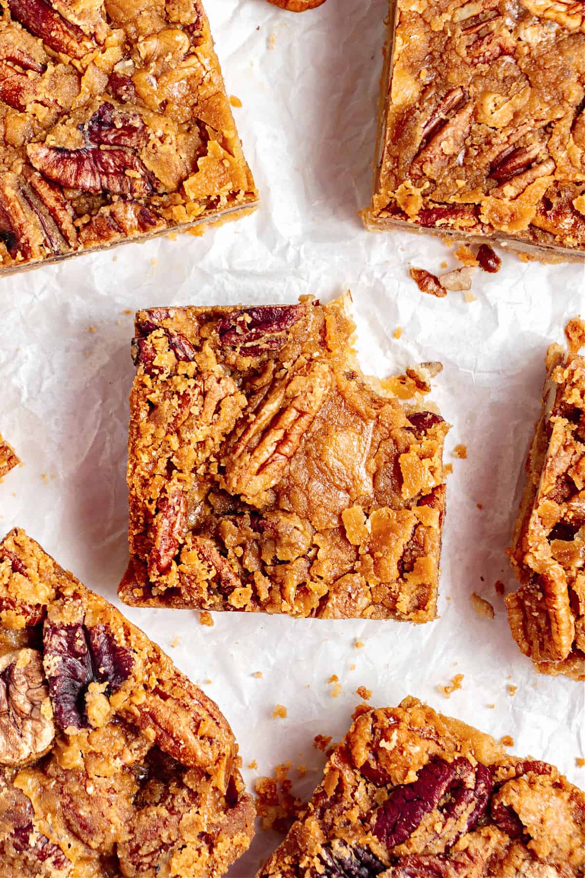 Several maple pecan bars on white paper, one is bitten. Top view.