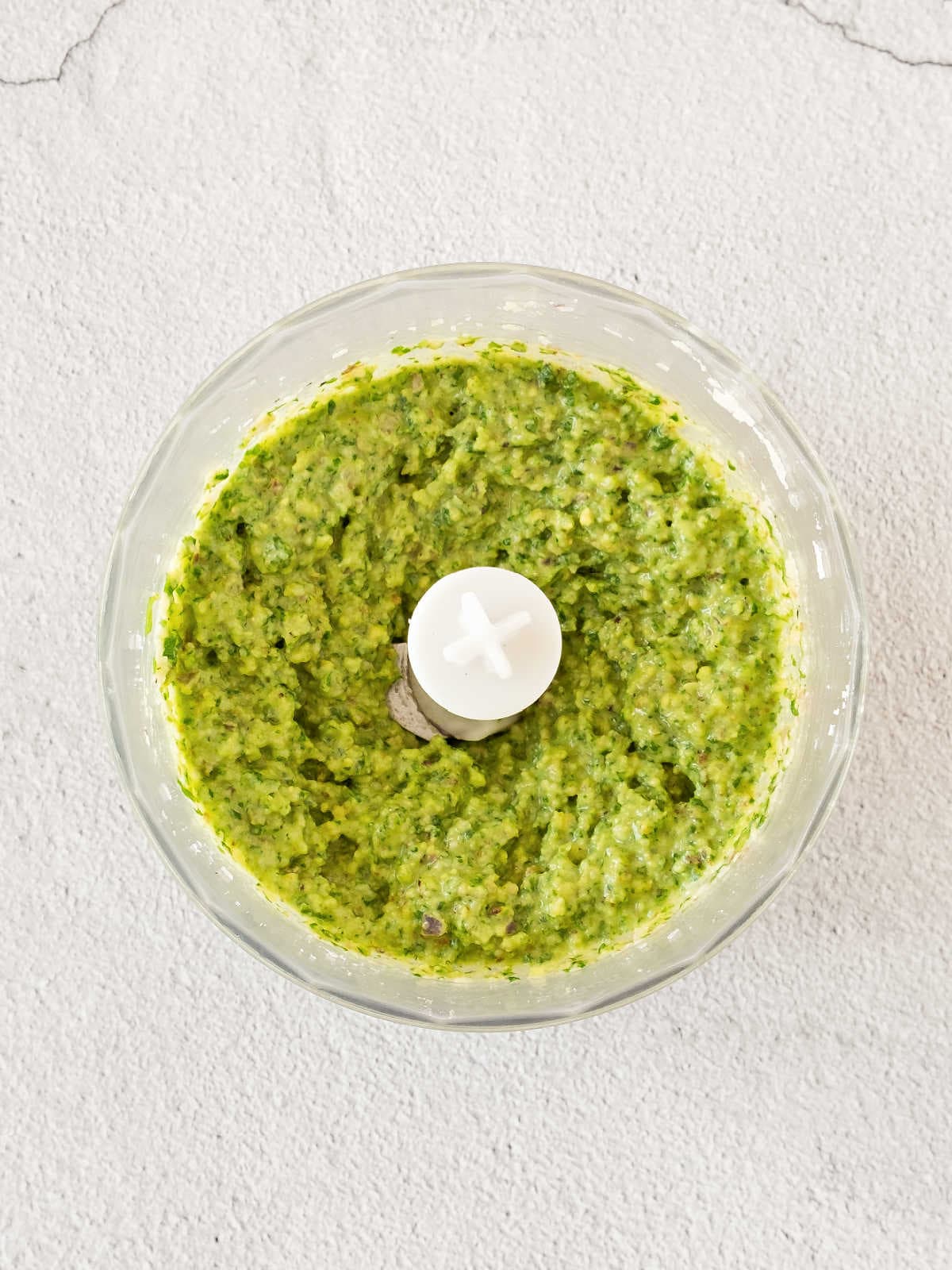 Food processor bowl with pesto. Top view. Gray background.