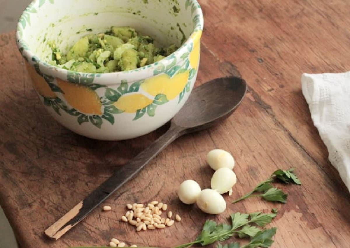 Yellow green bowl with potato salad on a wooden table with wooden spoon, quail eggs, pine nuts, parsley. 