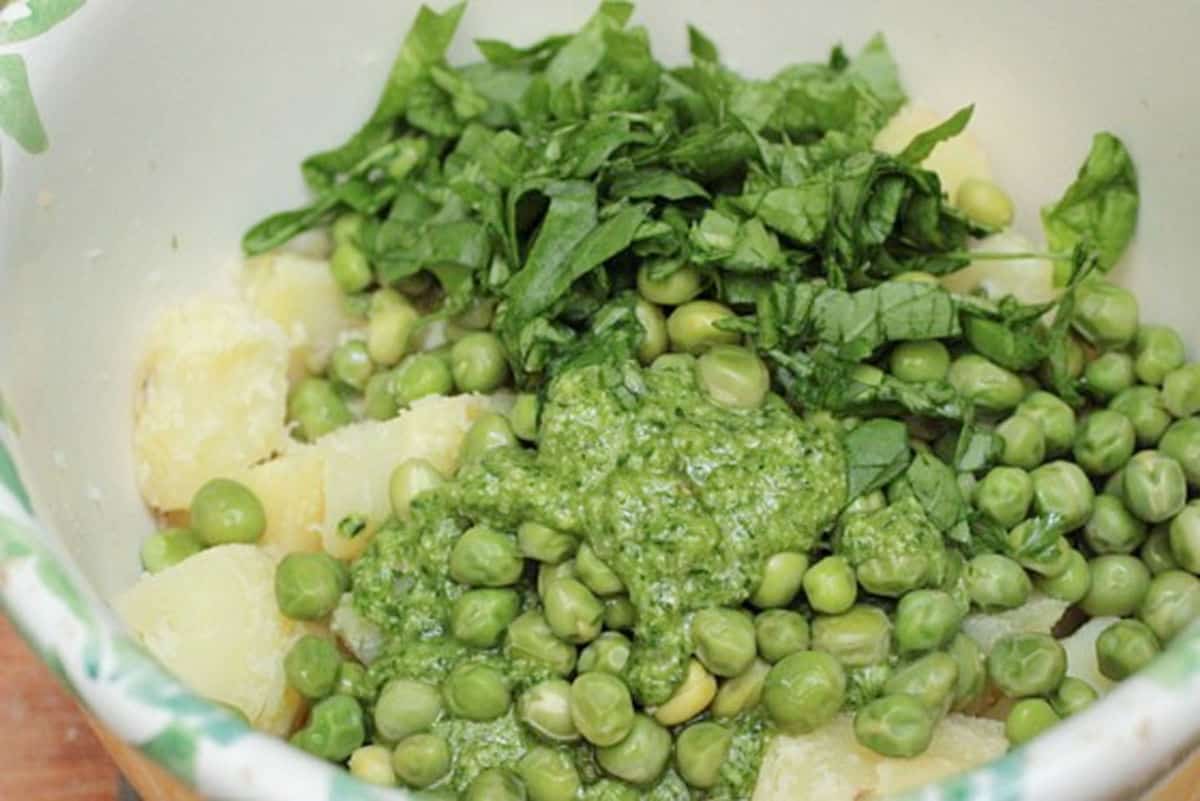 Pesto, peas, potato pieces, and basil in a salad bowl. 