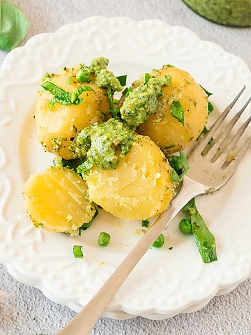 White plate with silver fork and potato pesto salad. Light gray surface.