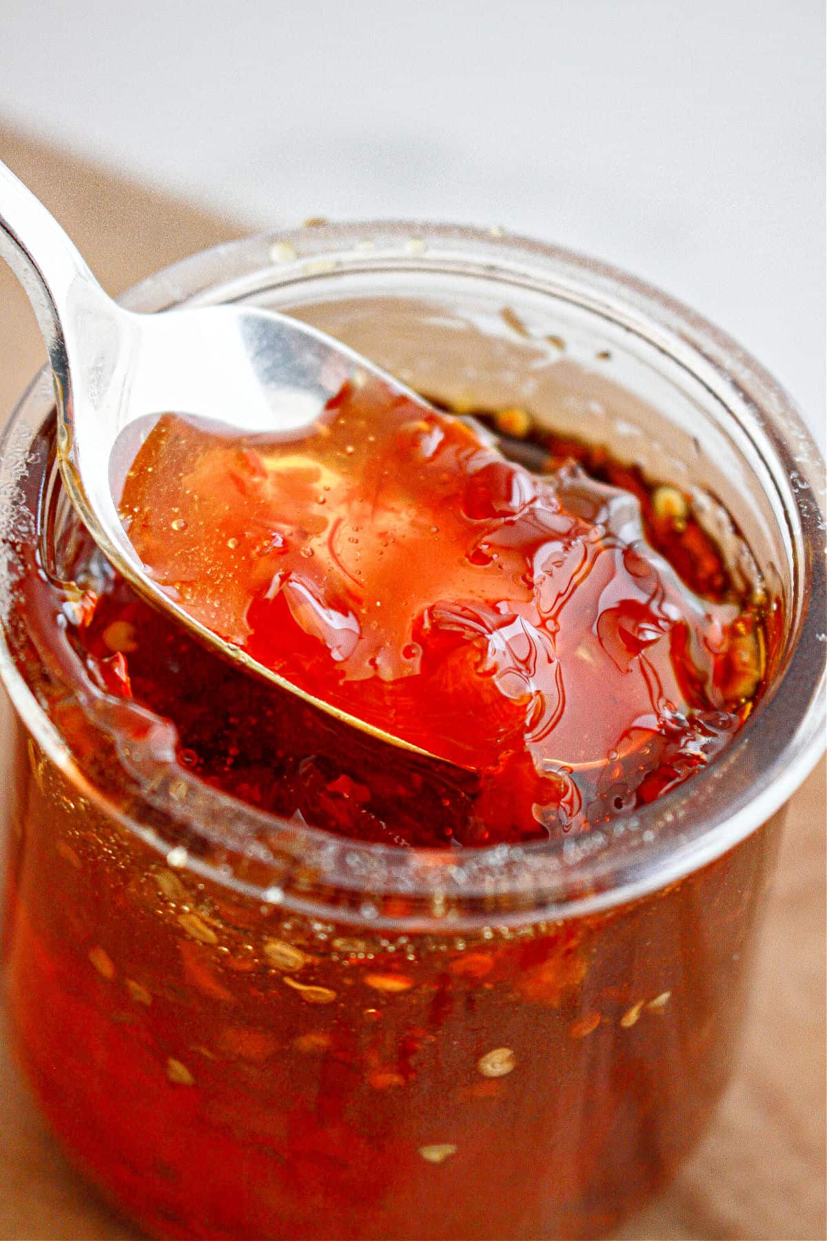 Jar with red chili jam being lifted with a spoon.