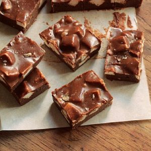 Top view of pieces of chocolate Marshmallow Fudge on white paper on a wooden table.