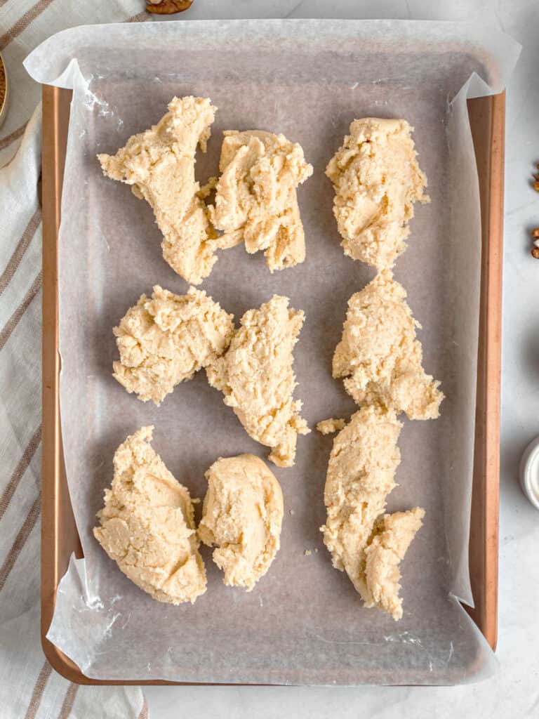 Mounds of shortbread crust on parchment-lined rectangular copper pan. Top view. 