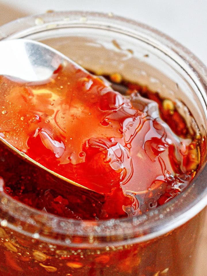 Close up of silver spoon with chili jam in a glass jar.