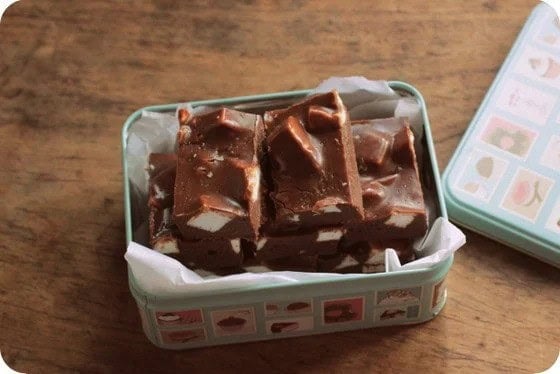 Blue tin with chocolate marshmallow fudge pieces on a wooden table.