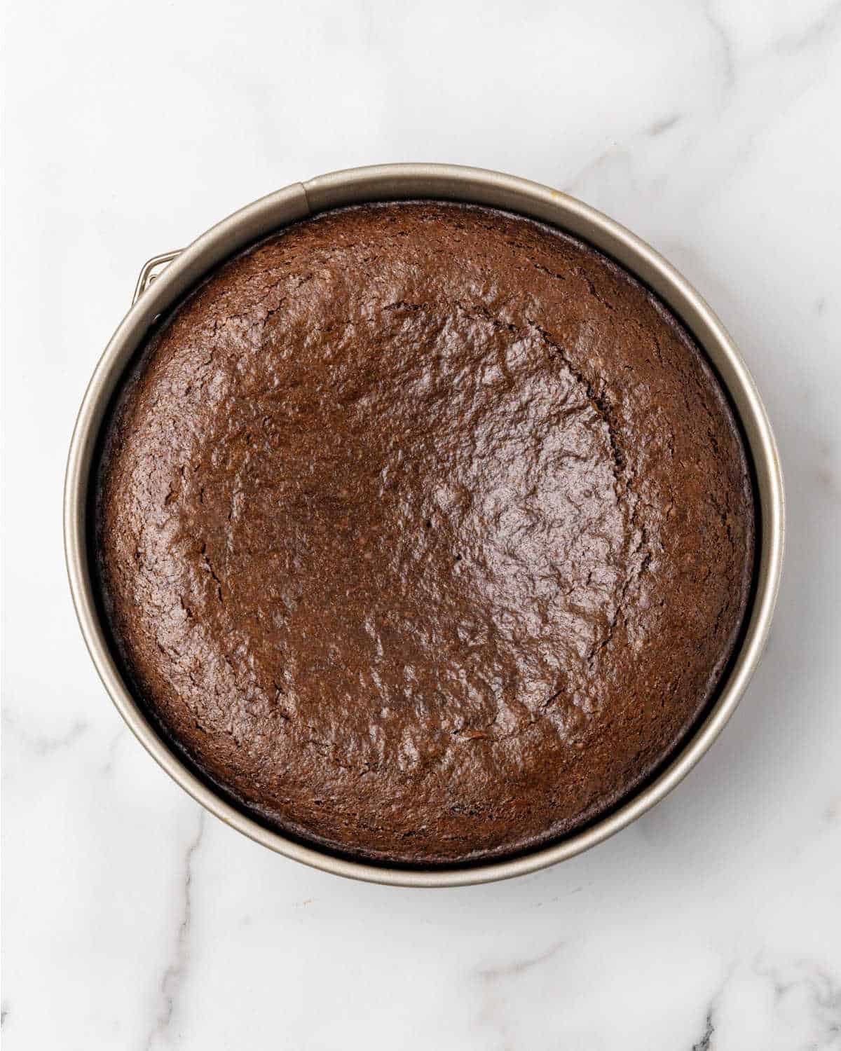 Baked chocolate cake in a metal round pan on a white marble surface.