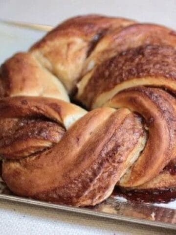 Baked wreath of cinnamon challah bread on a metal pan with white parchment paper.