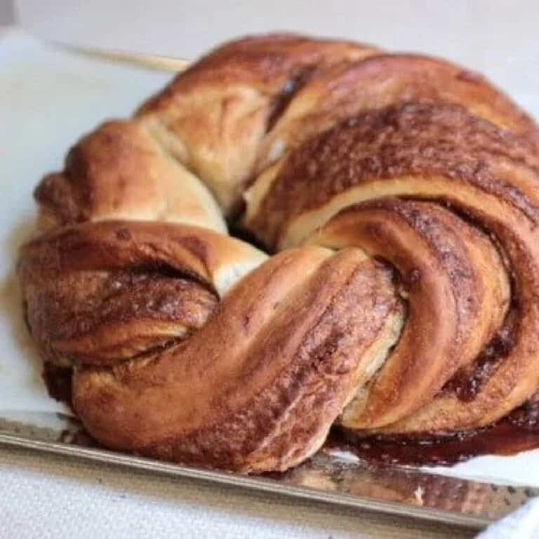 Baked wreath of cinnamon challah bread on a metal pan with white parchment paper.