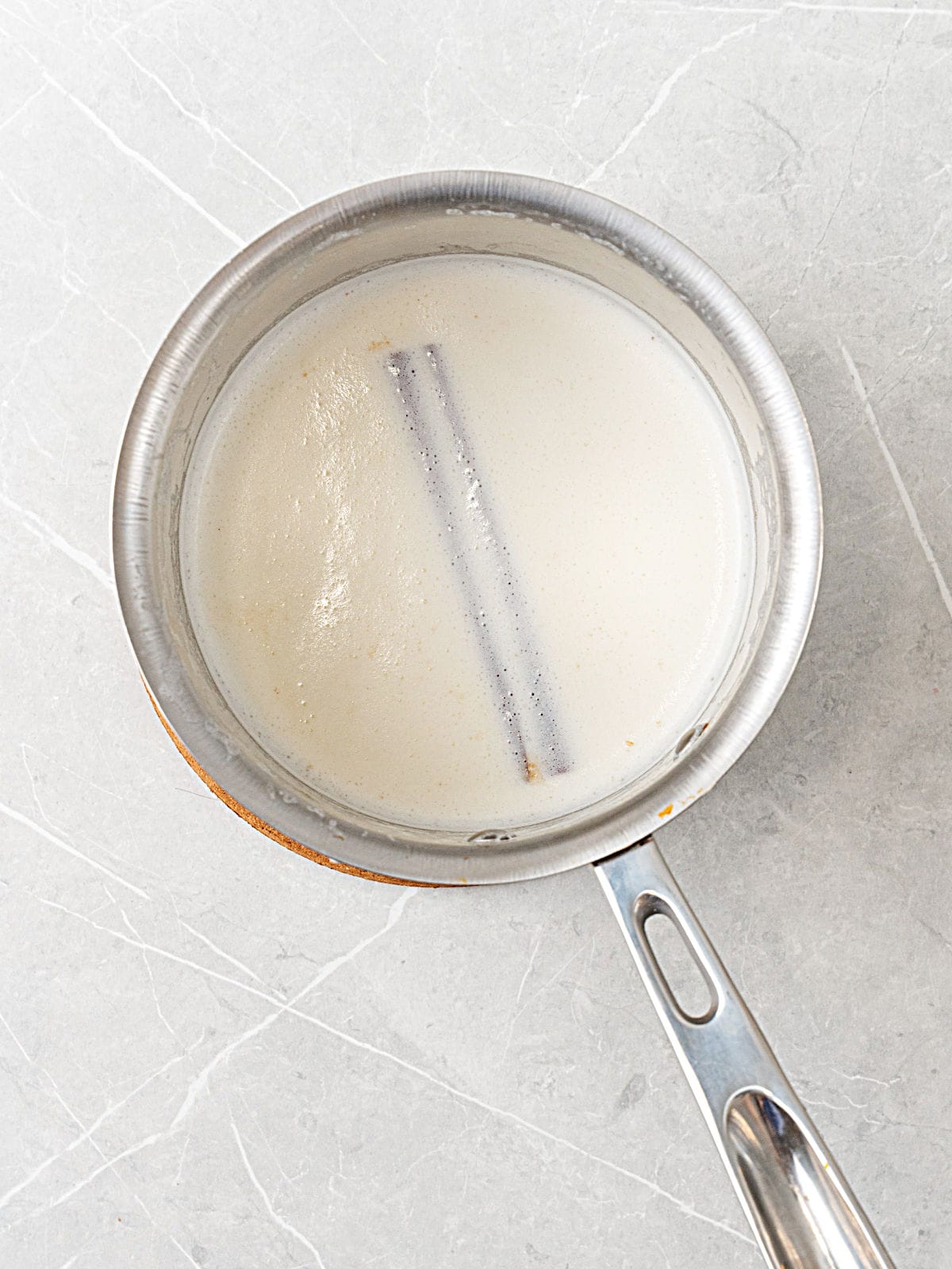 Saucepan with simmering milk with cinnamon stick. Light gray surface.