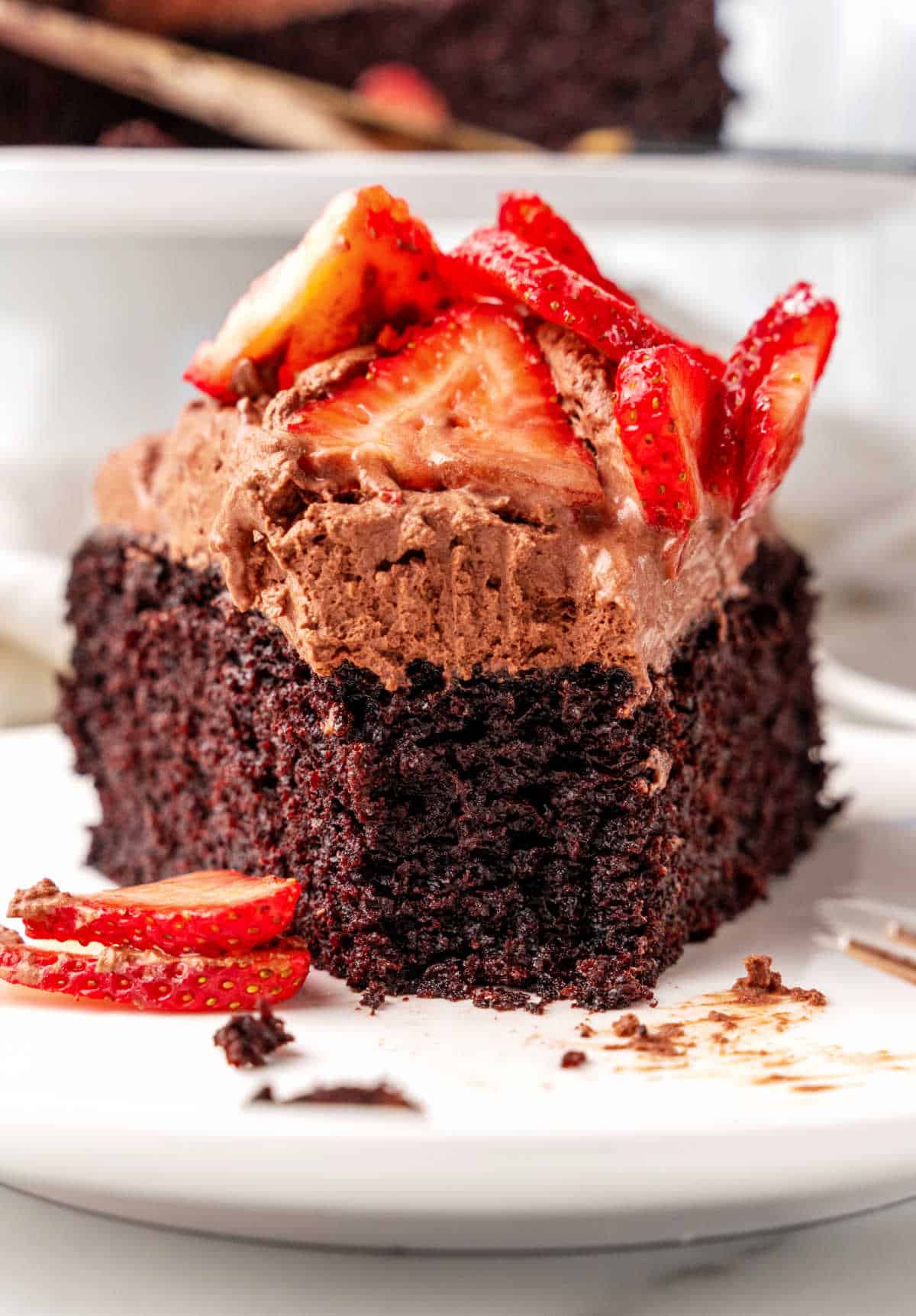 Front view of eaten slice of chocolate mousse cake with strawberries on a white plate. 