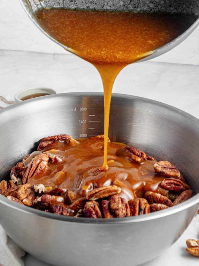 Pouring maple caramel onto a metal bowl with pecans. 