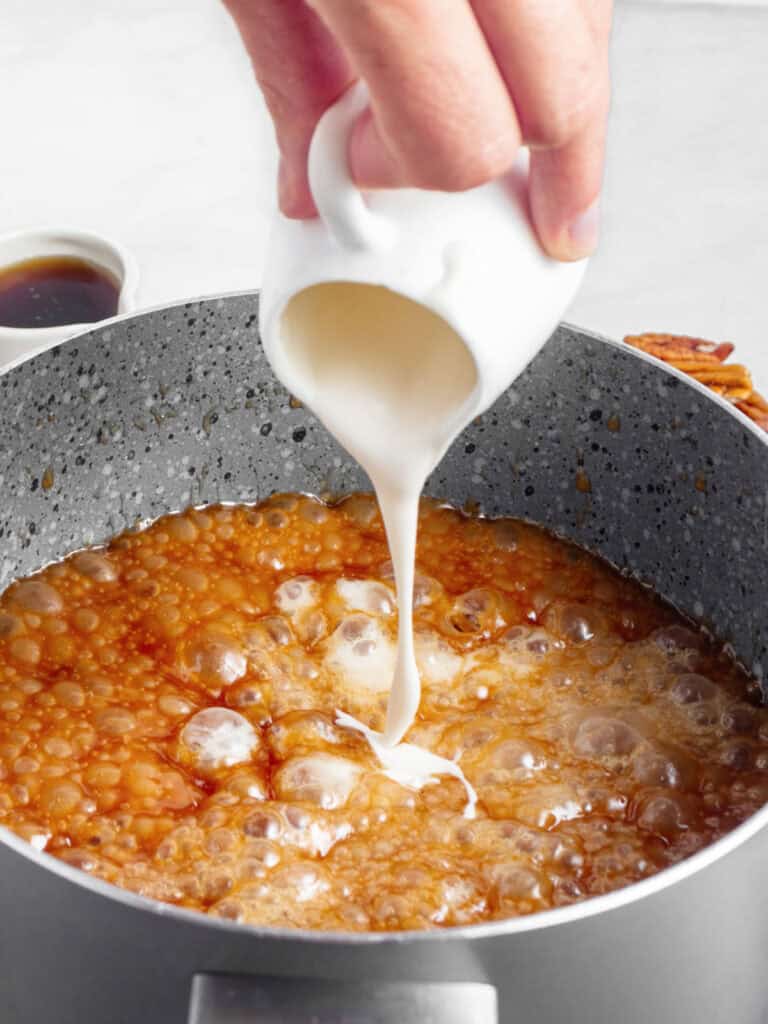 Cream being added to caramel maple mixture in a gray saucepan.