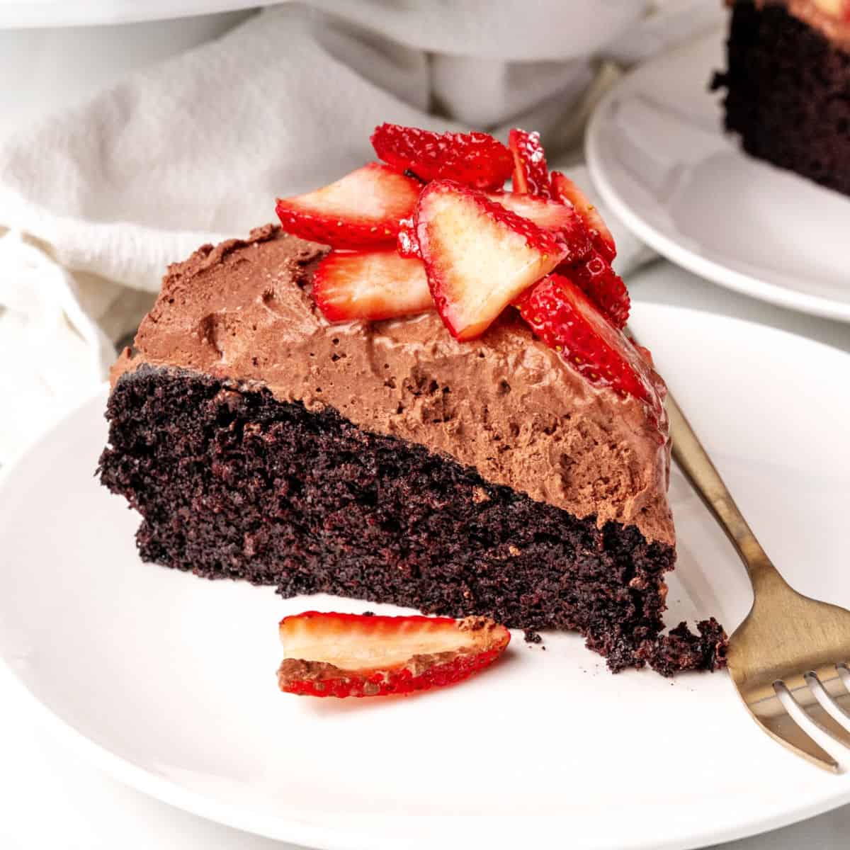 Slice of strawberry topped chocolate mousse cake on a white plate with a fork.