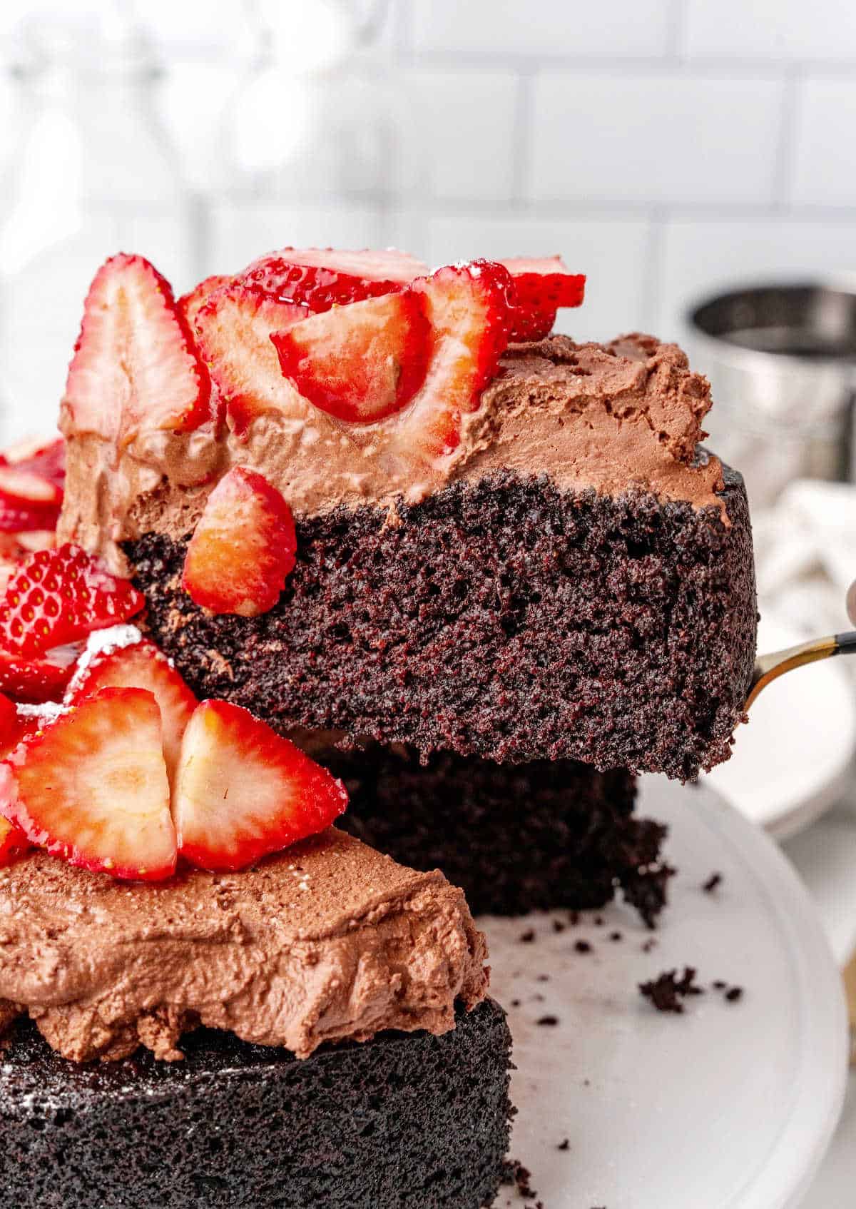 Slice of chocolate mousse cake with strawberries being lifted from whole cake.
