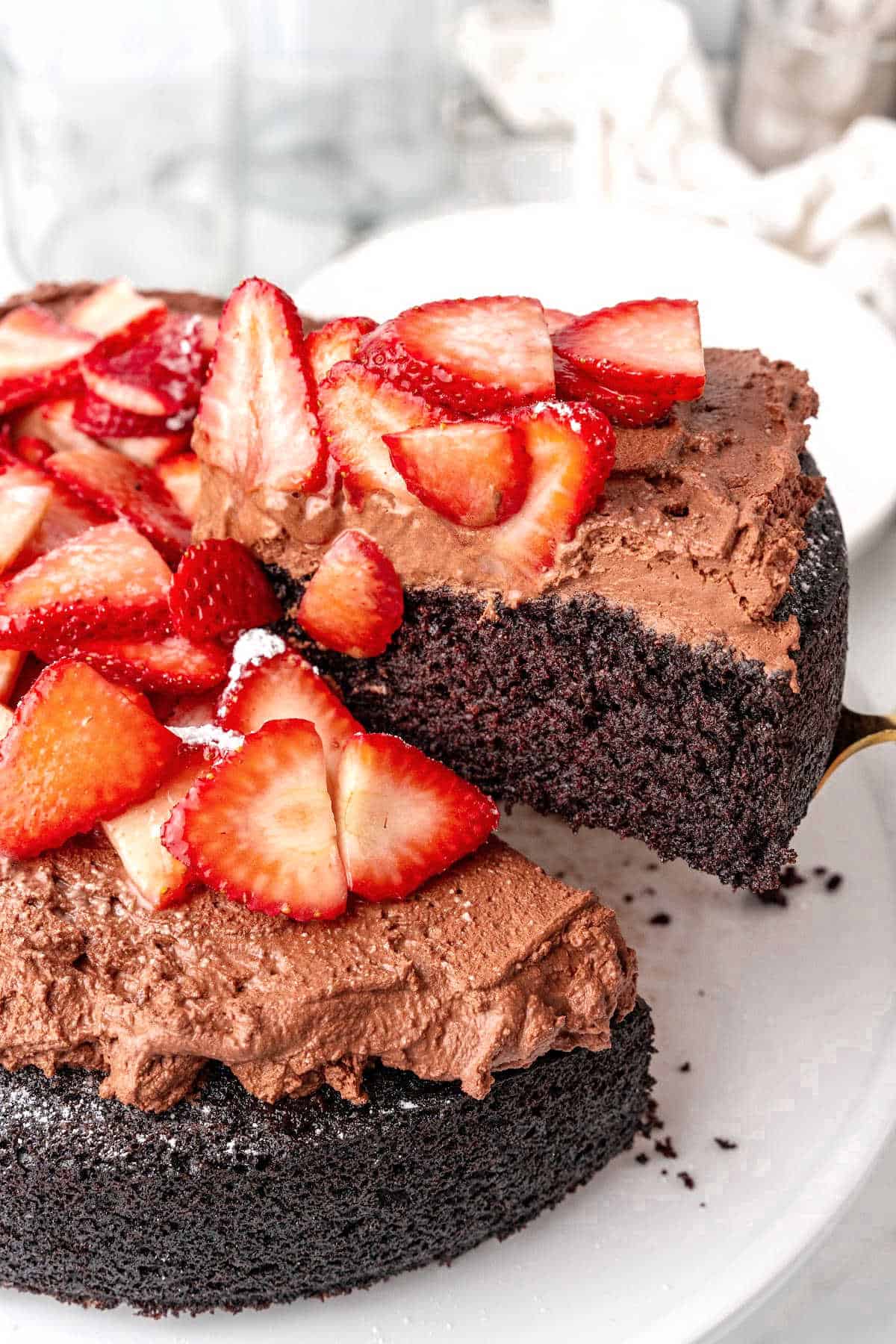 Strawberry topped chocolate mousse cake on a white cake stand with a slice being lifted.