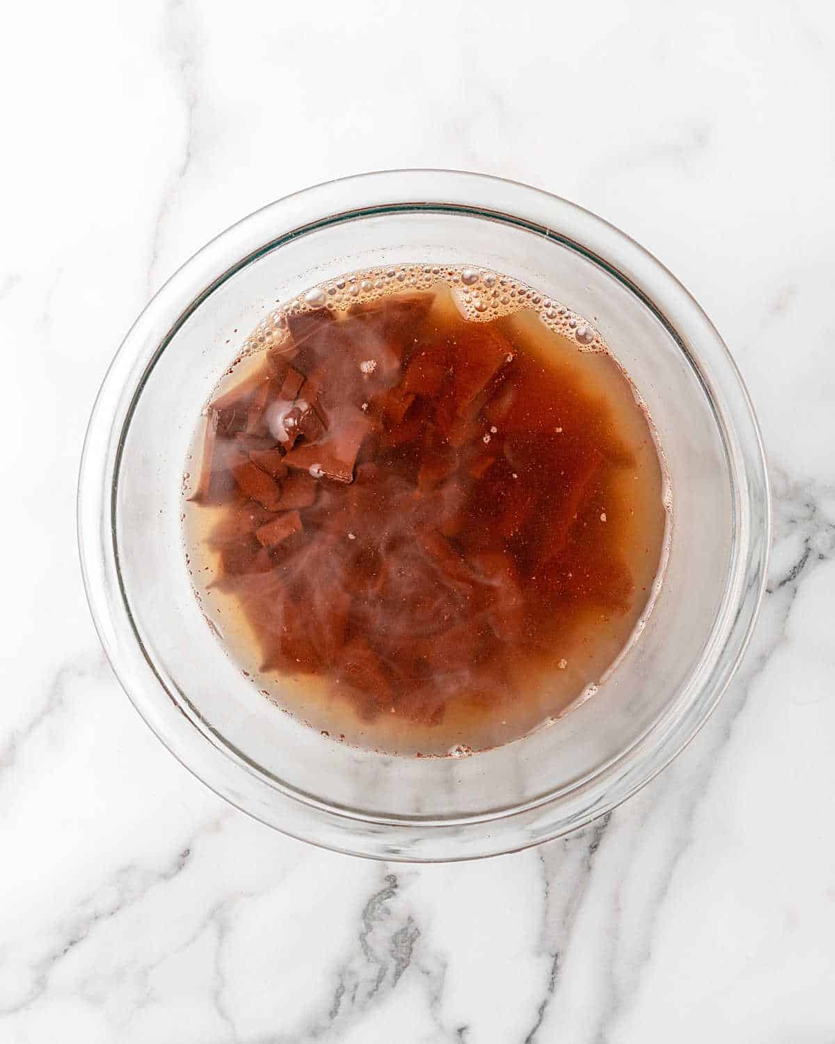 Glass bowl with chocolate pieces and water on a white marble surface.