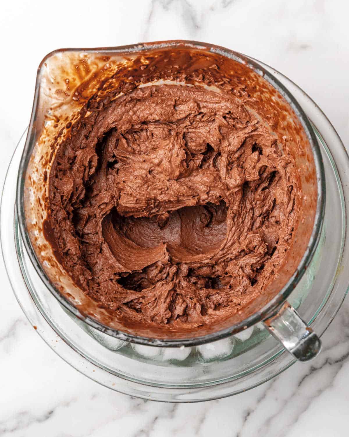 Chocolate mousse in a glass jar over a glass bowl with ice. White marble surface.