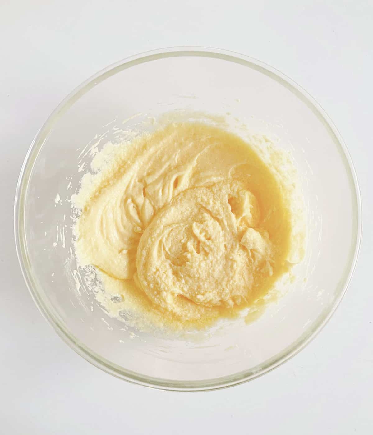 Creamed butter and sugar in glass bowl on a white surface.