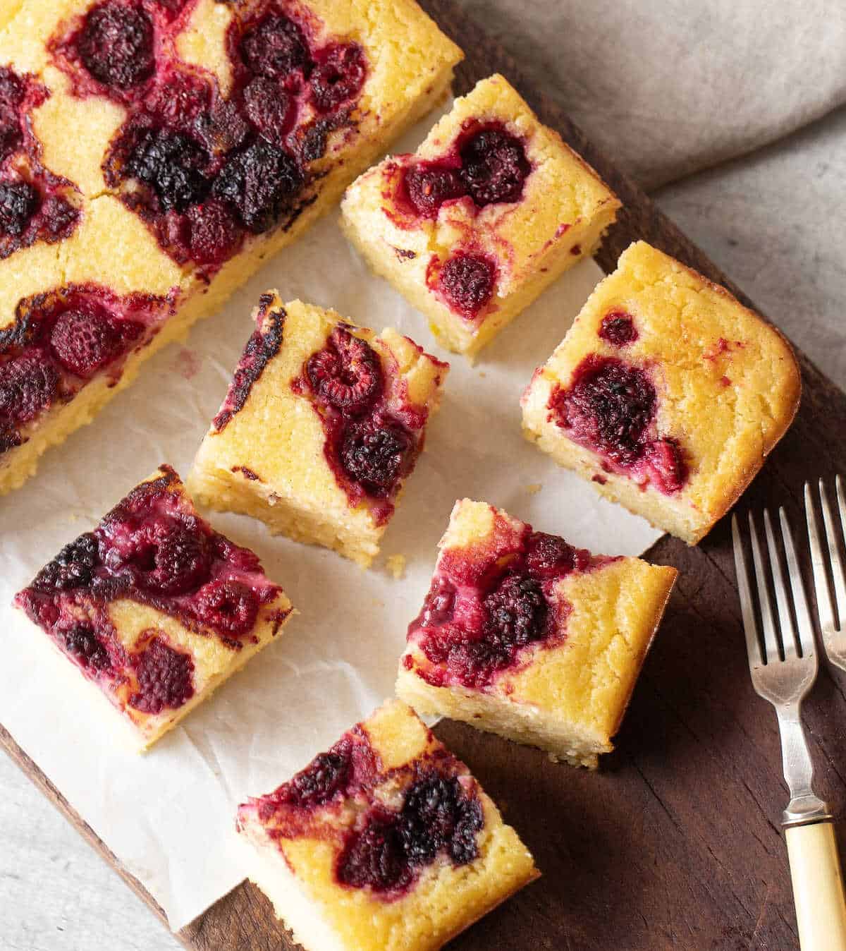 Close up overview of berry ricotta squares on white paper and wooden board.