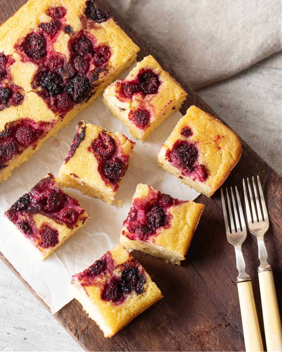 Top view of berry ricotta cake squares on wooden board, two forks.