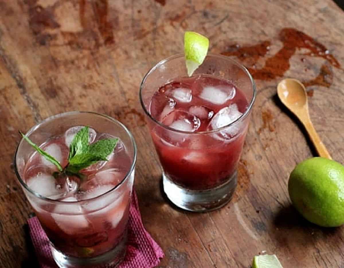 Top view of glasses with cherry cocktail and lime on wooden table.