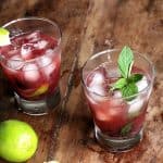 Wooden table with glasses of cherry cocktail, limes and mint sprigs