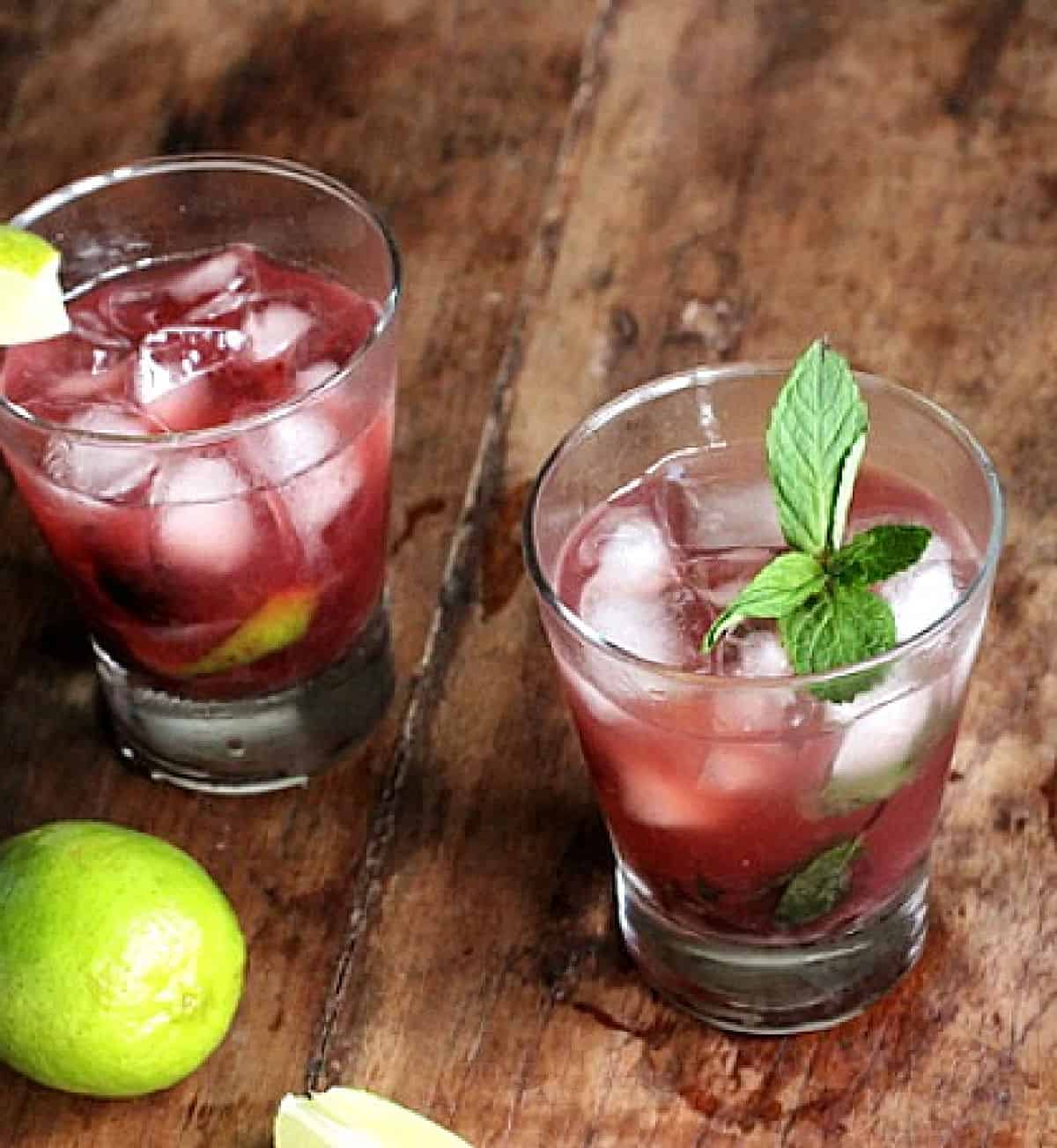 Wooden table with glasses of cherry cocktail, limes and mint sprigs.