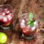 Wooden table with glasses of cherry cocktail, limes and mint sprigs.