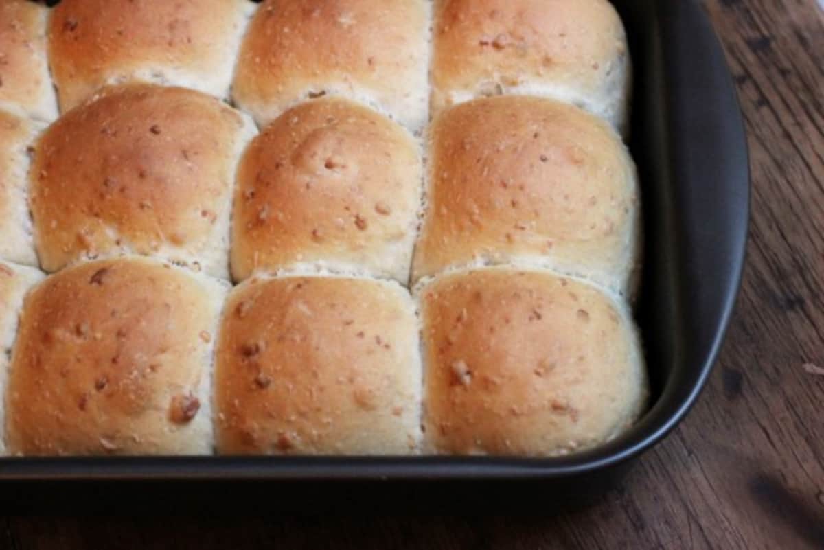 Baked golden buns on a rectangular dark metal pan on a wooden table. 