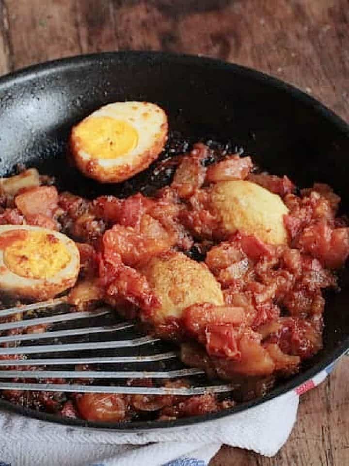 Golden eggs with tomato sauce in a dark skillet with spatula. Wooden table.