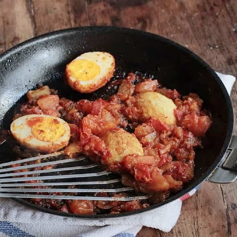 Golden eggs with tomato sauce in a dark skillet with spatula. Wooden table.