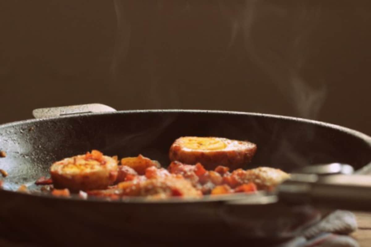 Frontal view of dark skillet with hard-boiled egg halves and tomato sauce. Dark background. 