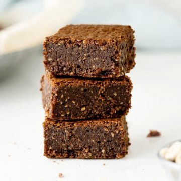 Close up stack of three gluten-free hazelnut brownies on a white surface.