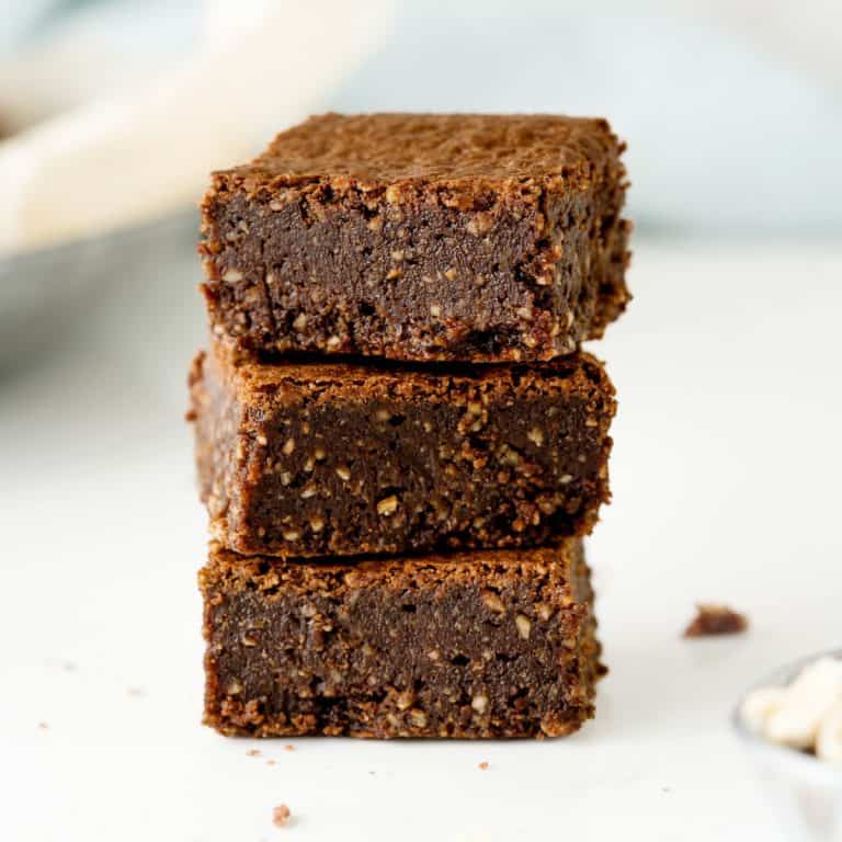 Close up stack of three brownies on a white surface with light blue and cream colored background.