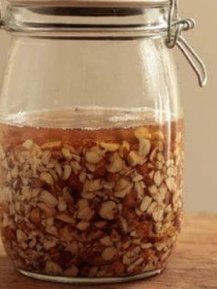 Close up of mason jar with with chopped hazelnut and vodka. Wooden surface.