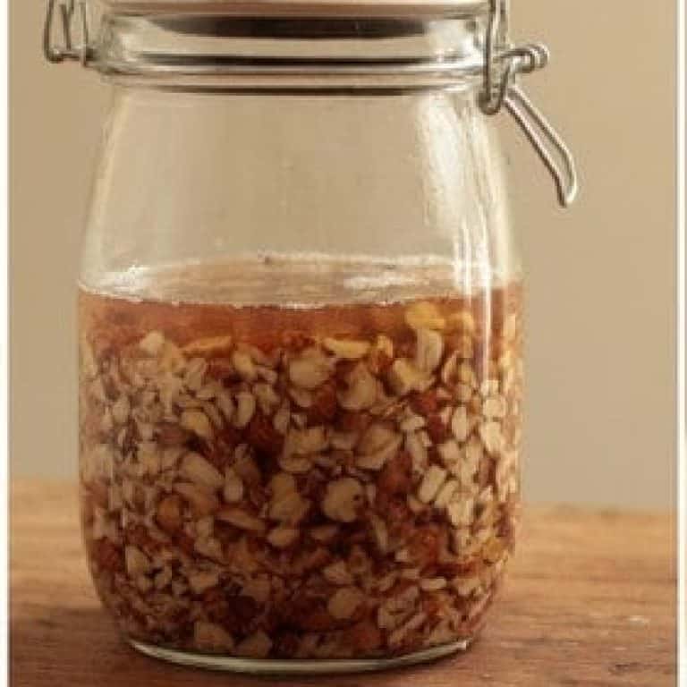 Close up of mason jar with with chopped hazelnut and vodka. Wooden surface.