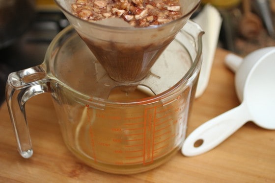 A colander with hazelnut liqueur dripping over a glass jar on a wooden board.