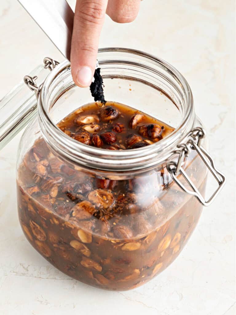 Vanilla seeds being added to mason jar with hazelnut liqueur. White background.