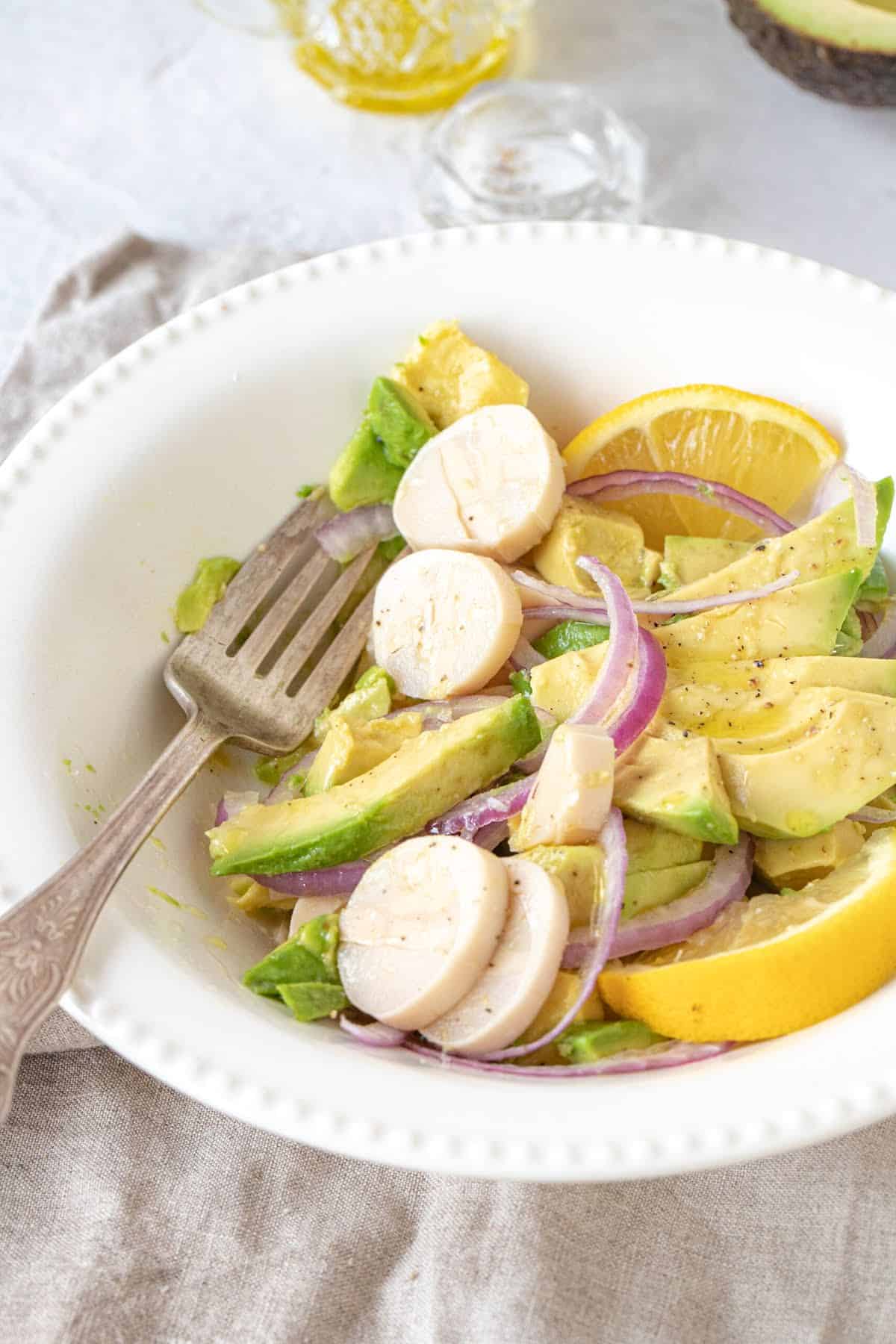 Eaten salad with avocado, heart of palm and red onion in a white plate with silver fork. 