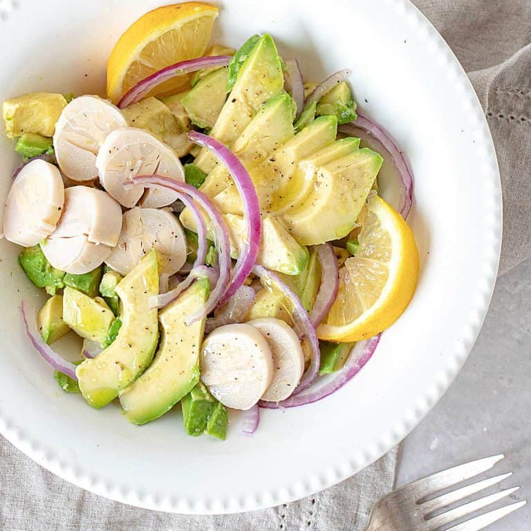 White bowl plate with avocado, heart of palm and red onion salad on a grey surface.