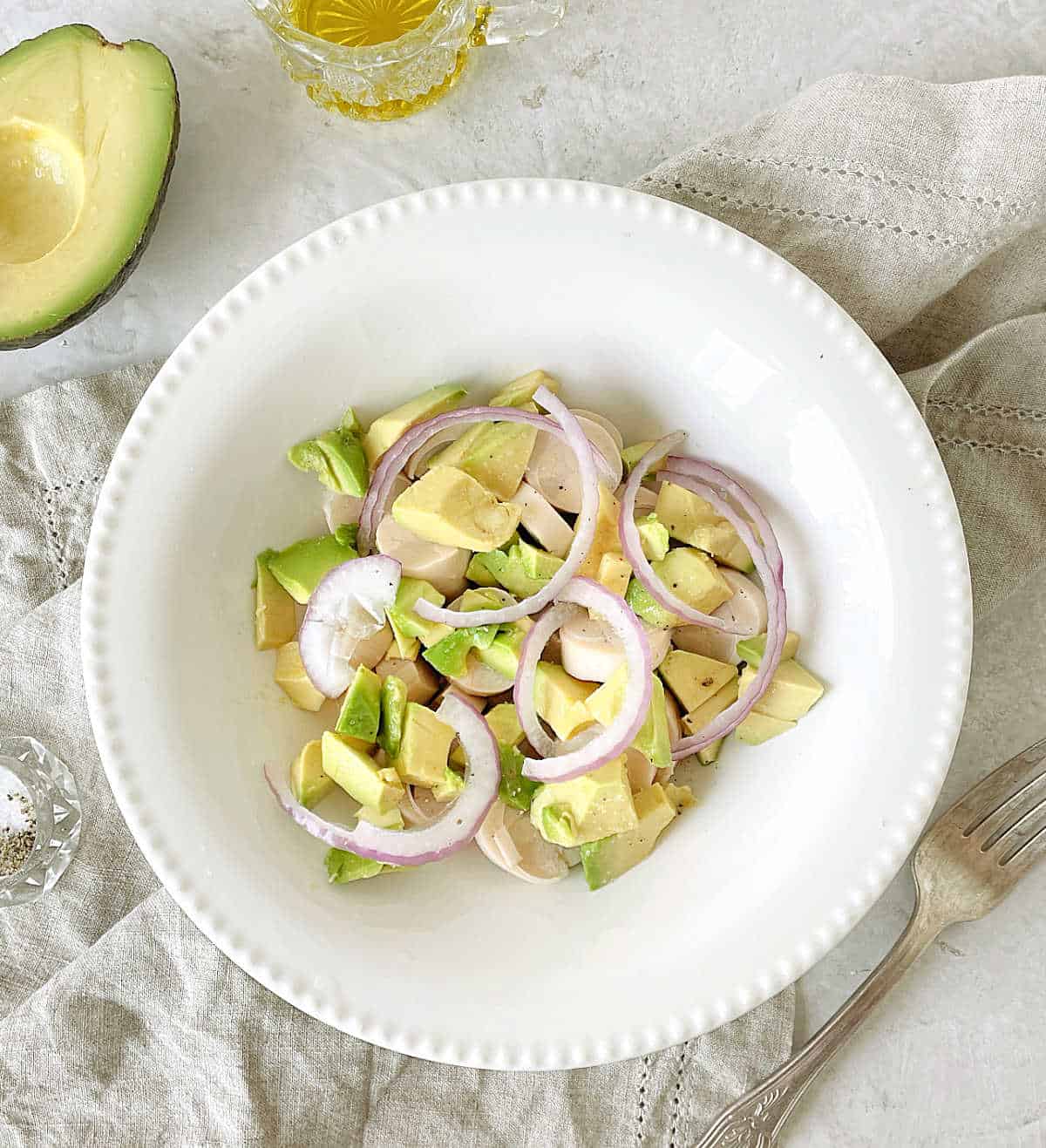 Layer of avocado, red onion, and heart of palm salad in a white plate on a grey surface.