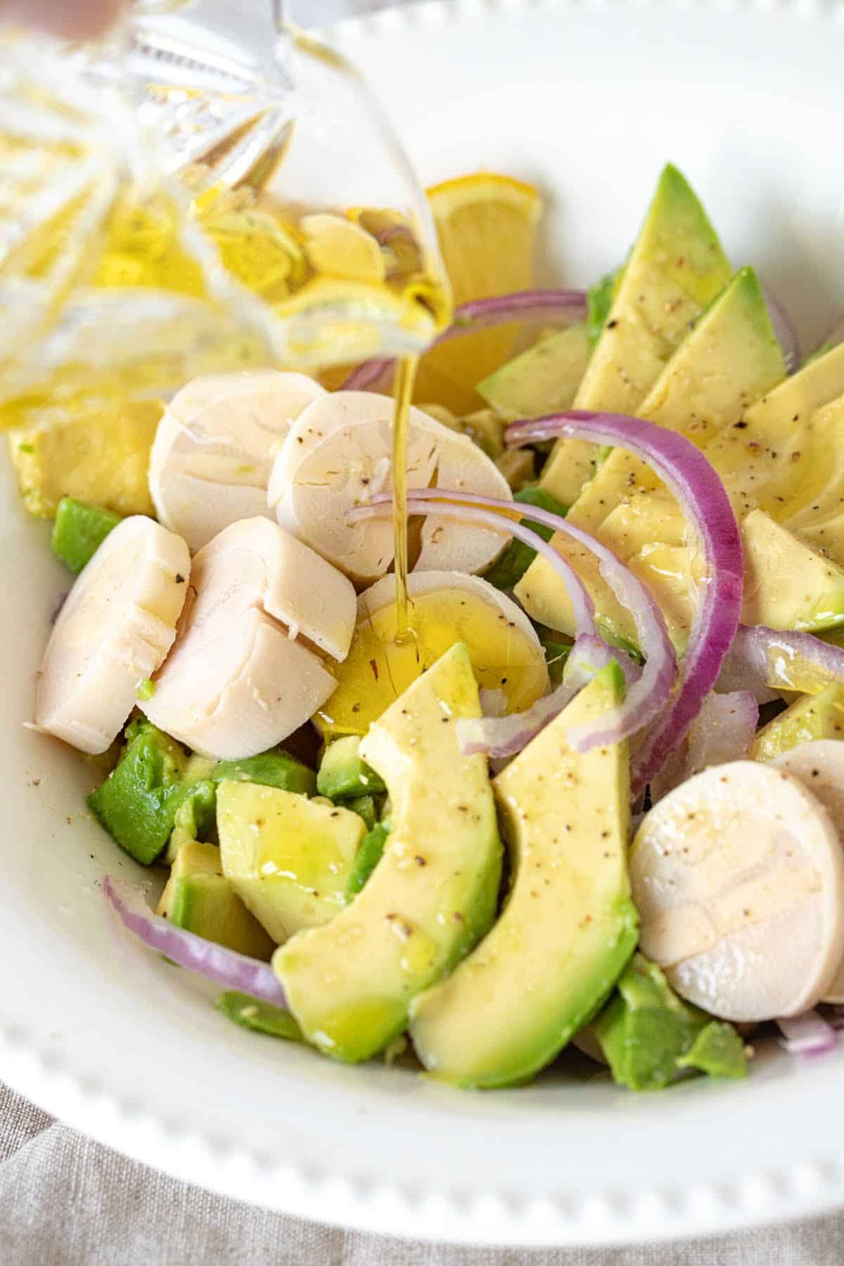 Dressing being poured over avocado, heart of palm salad on a white plate. 